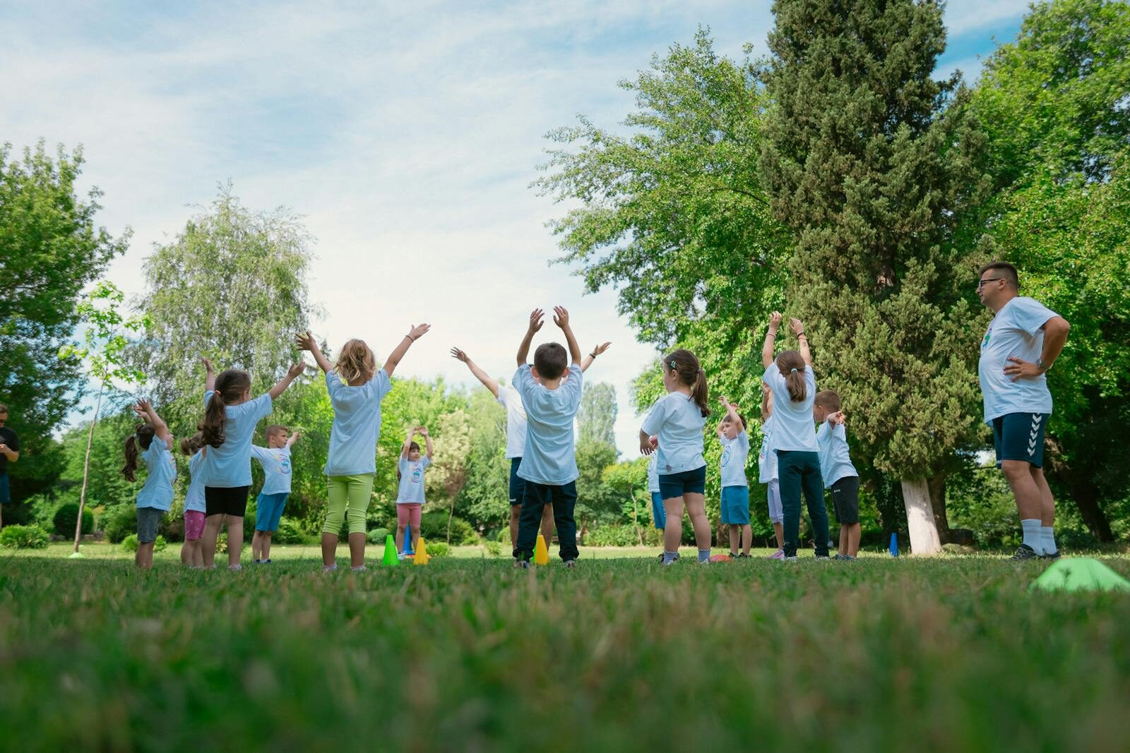 Group of children with instructor doing exercises in a sunny park setting, promoting outdoor activity.