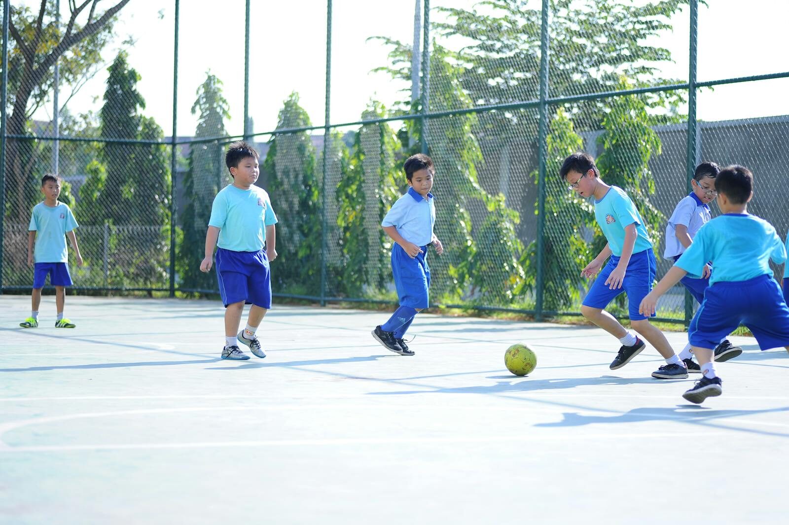 A group of boys playing soccer on an outdoor court under the bright day.